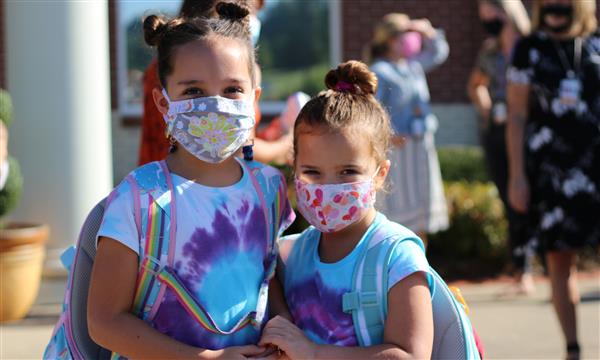 two girls smile while wearing mask